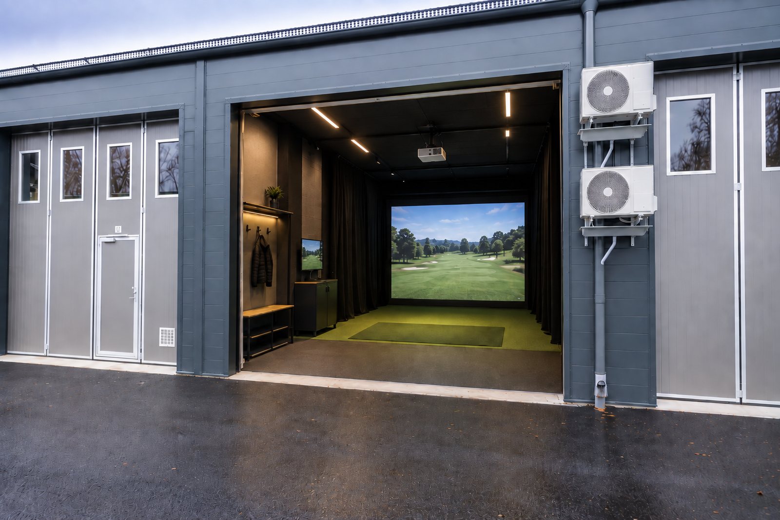 Öppen garageport in till simulatorn: skärm med golfbana, projektor i taket, hängare och slagmatta.
